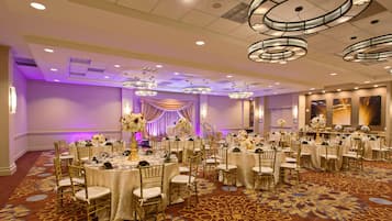 A banquet hall with round tables, gold chairs, and a patterned carpet.