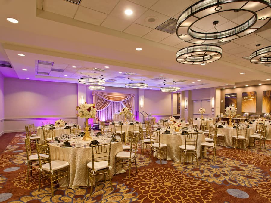 A banquet hall with round tables, gold chairs, and a patterned carpet.