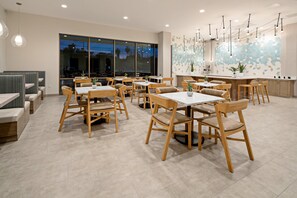 Un espace de restauration moderne avec des tables et des chaises en bois, de grandes fenêtres et un mur décoratif.
