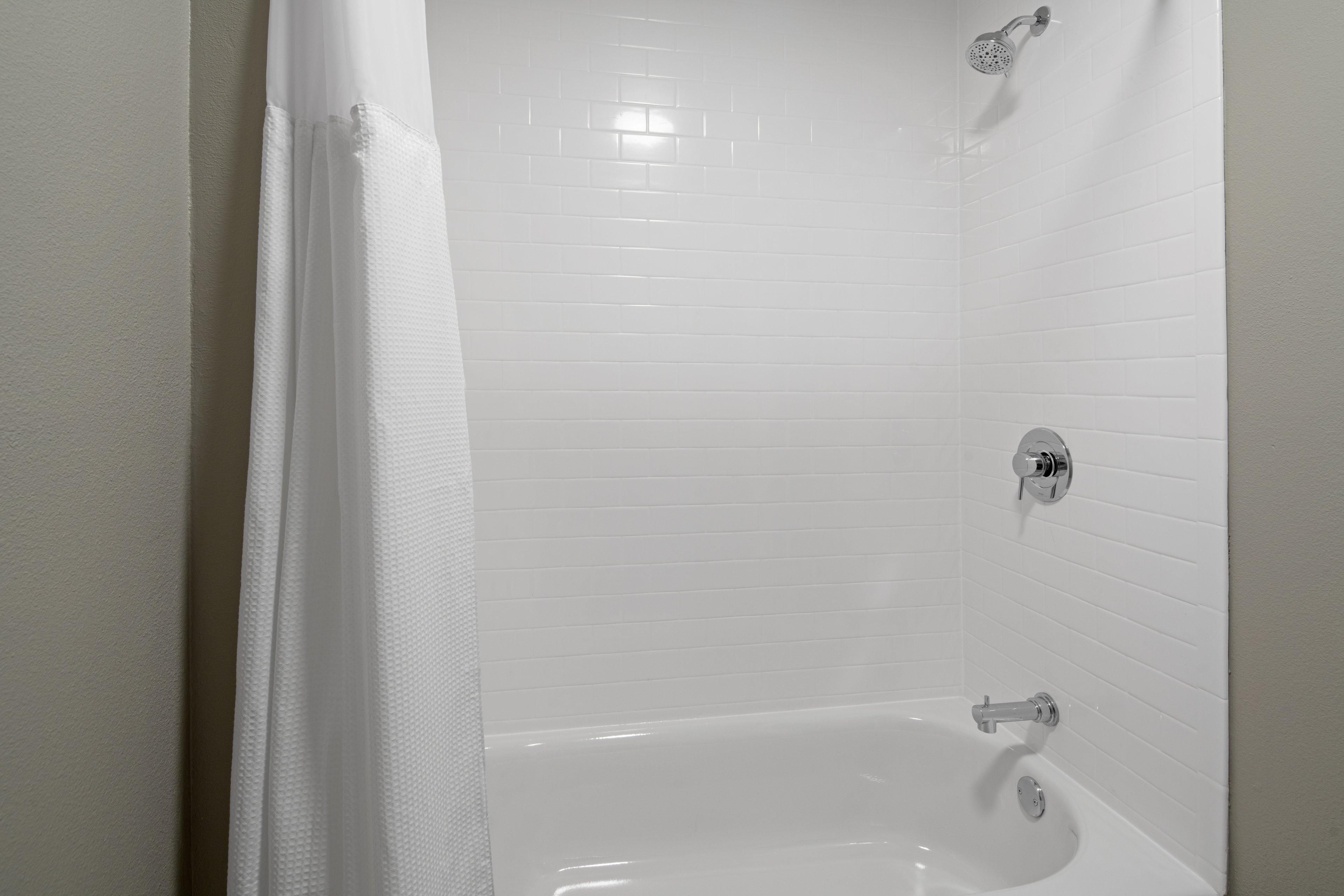 A white tiled shower area with a showerhead and a faucet.