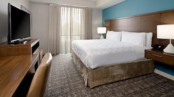 Una habitación de hotel con cama, televisor, escritorio, lámpara y ventana con cortinas.