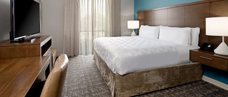 Una habitación de hotel con cama, televisor, escritorio, lámpara y ventana con cortinas.