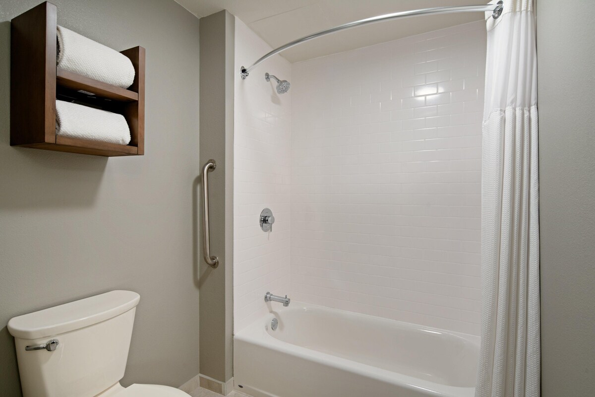 Een badkamer met een wit toilet, een douche met glazen deur en een houten plank met handdoeken.
