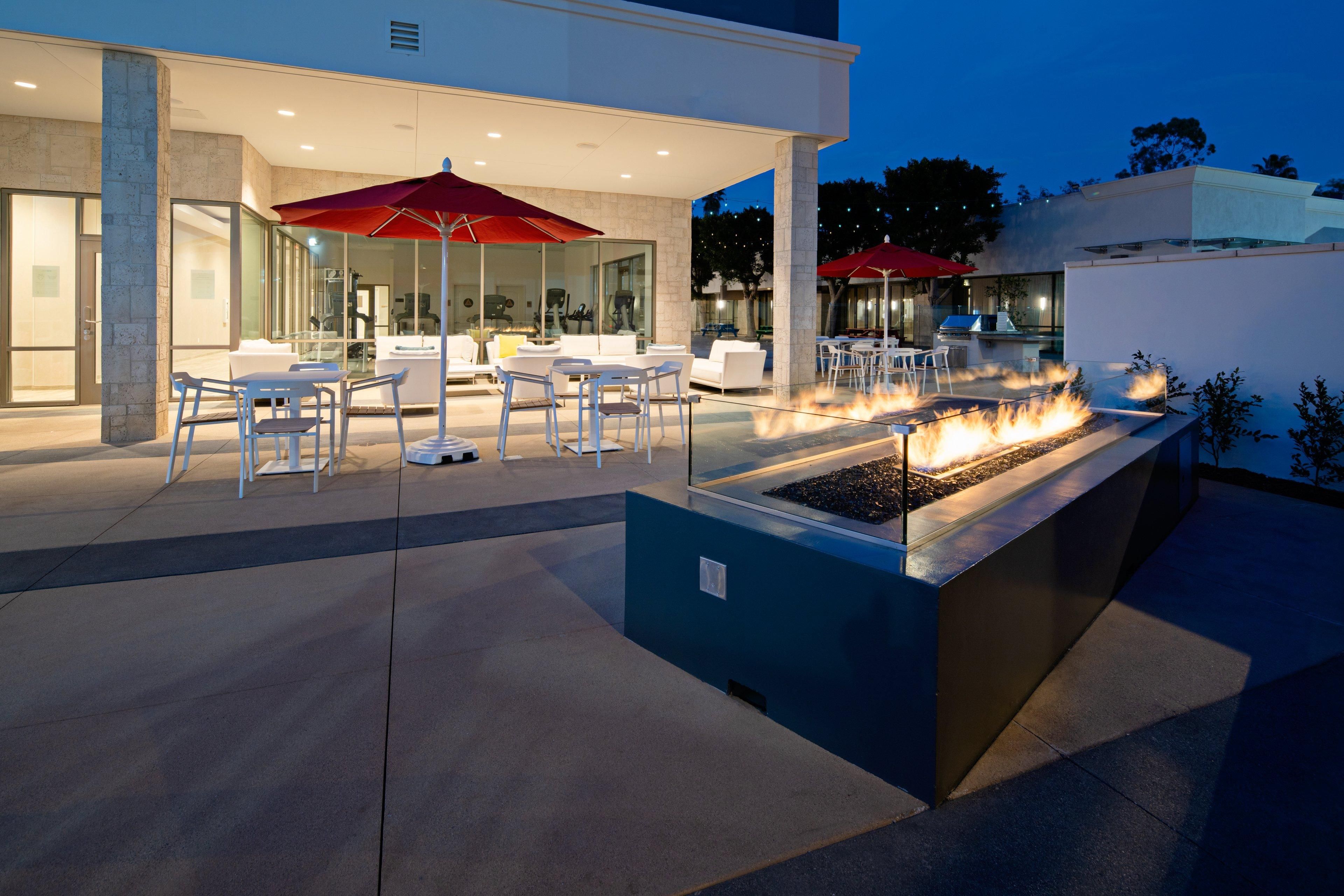 An outdoor patio with seating, a fire feature, and a modern building in the background.