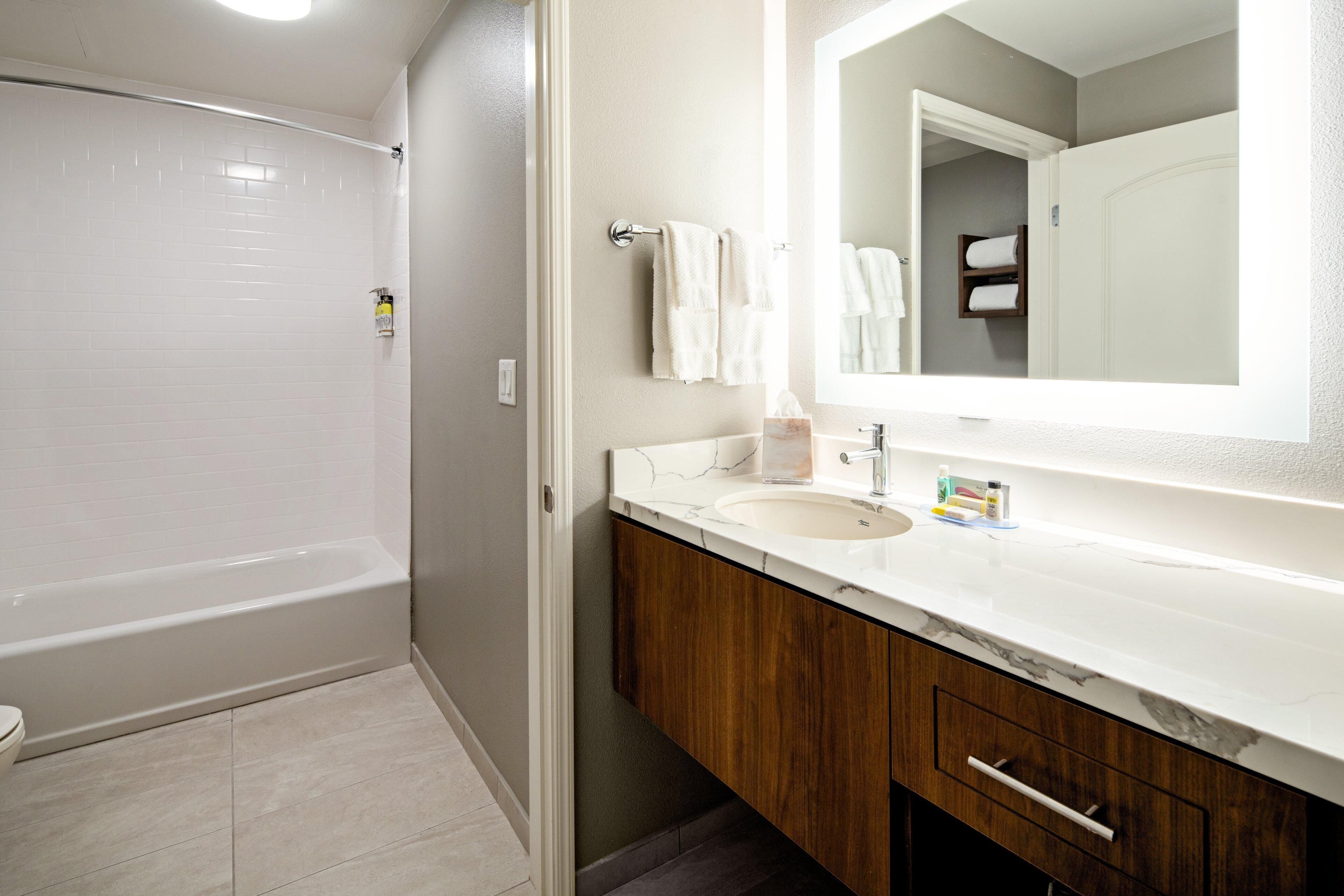 A bathroom with a bathtub, a sink with a mirror, and wooden cabinets.