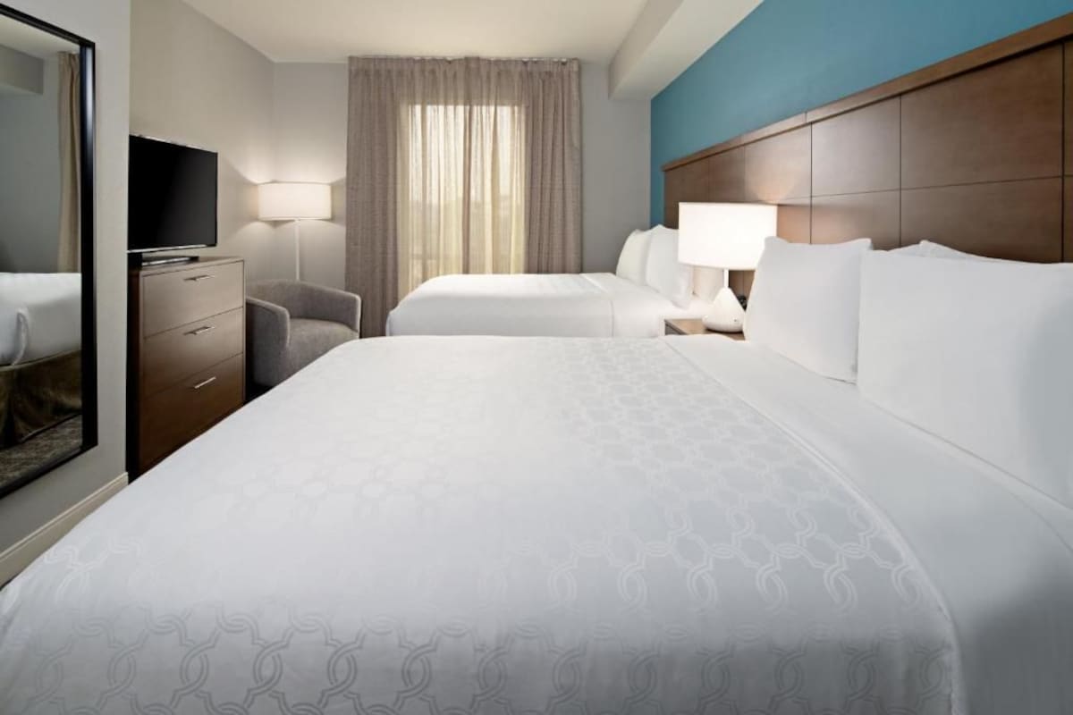 A hotel room with two beds, a television, a desk, and a chair.