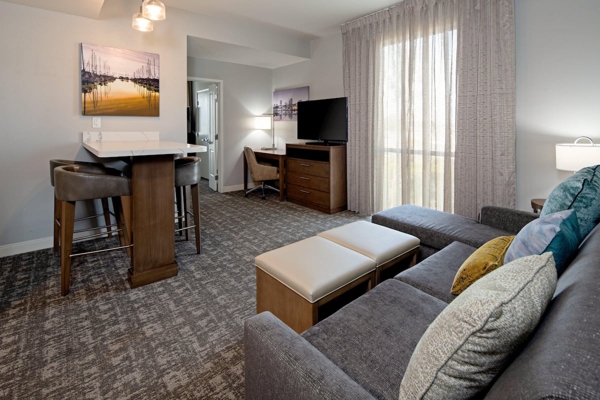 Quarto de hotel com sofá, escrivaninha com cadeira, televisão e um quadro na parede.