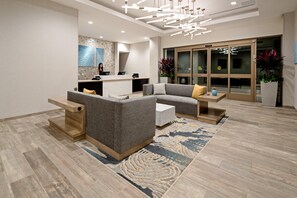 Un espace d’accueil moderne comprenant un comptoir de réception, un coin salon avec des canapés et un tapis à motifs.