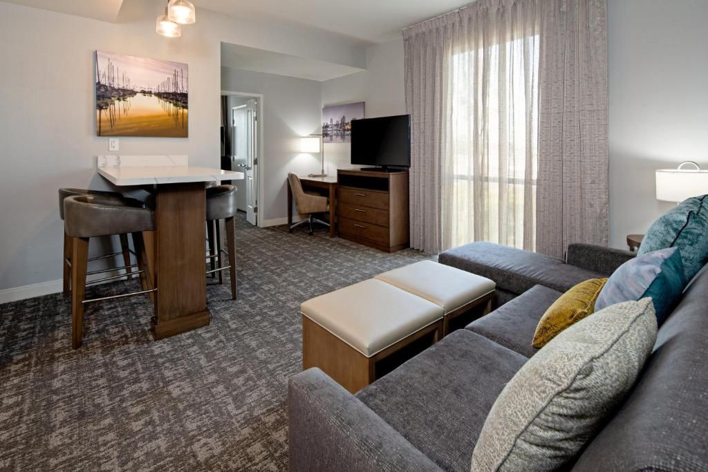 A hotel room with a sofa, a desk with a chair, a television, and a painting on the wall.