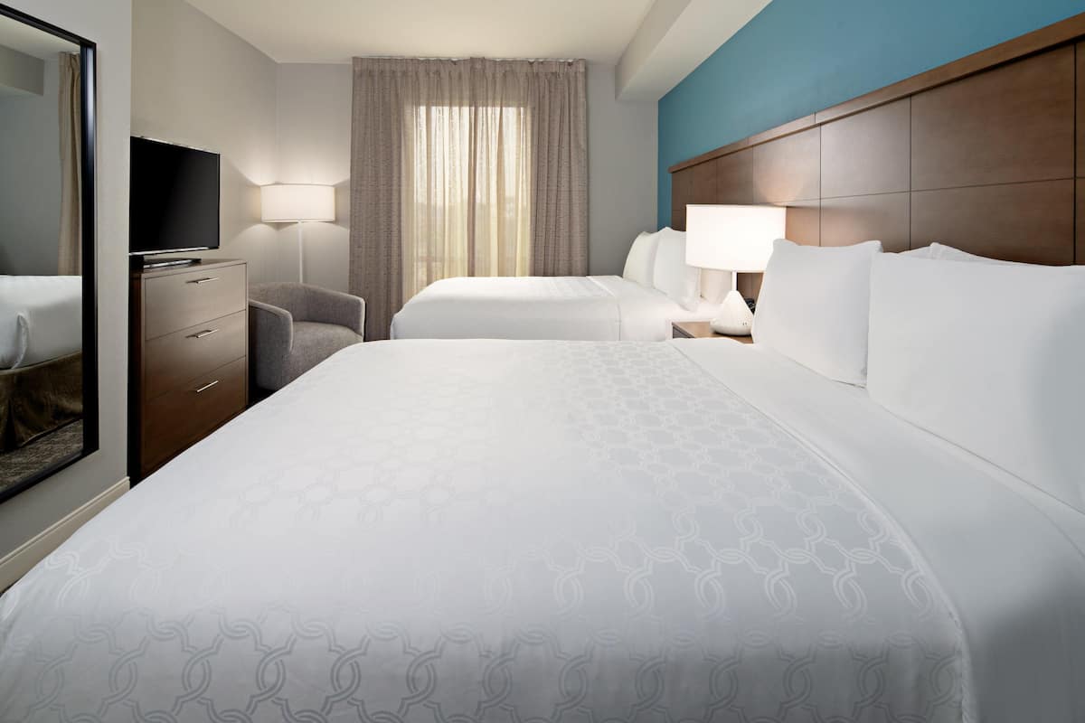 Quarto de hotel com duas camas, televisão, escrivaninha e uma cadeira.