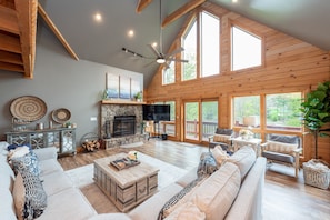 A spacious living room with a fireplace, comfortable seating, and large windows. - Family Lake Retreat w/ Fire Pit & Hot Tub (Swanton)