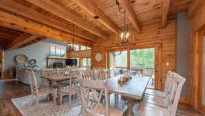 A wooden cabin interior with a dining area, kitchen, and large windows. - Family Lake Retreat w/ Fire Pit & Hot Tub (Swanton)