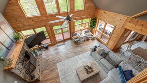 A spacious living room with a stone fireplace, wooden ceiling, and large windows. - Family Lake Retreat w/ Fire Pit & Hot Tub (Swanton)