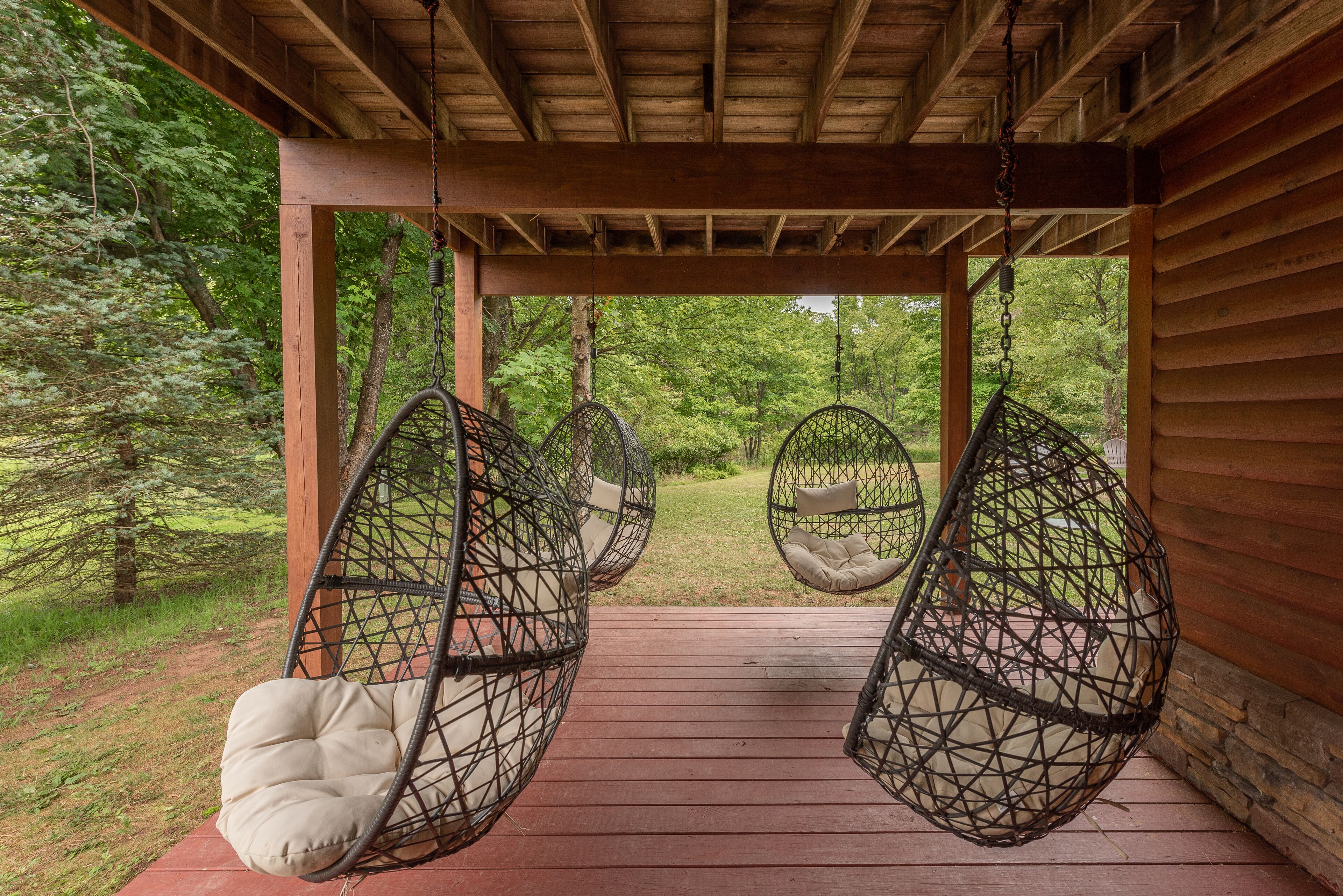 A wooden deck with three hanging chairs and a cushioned bench.