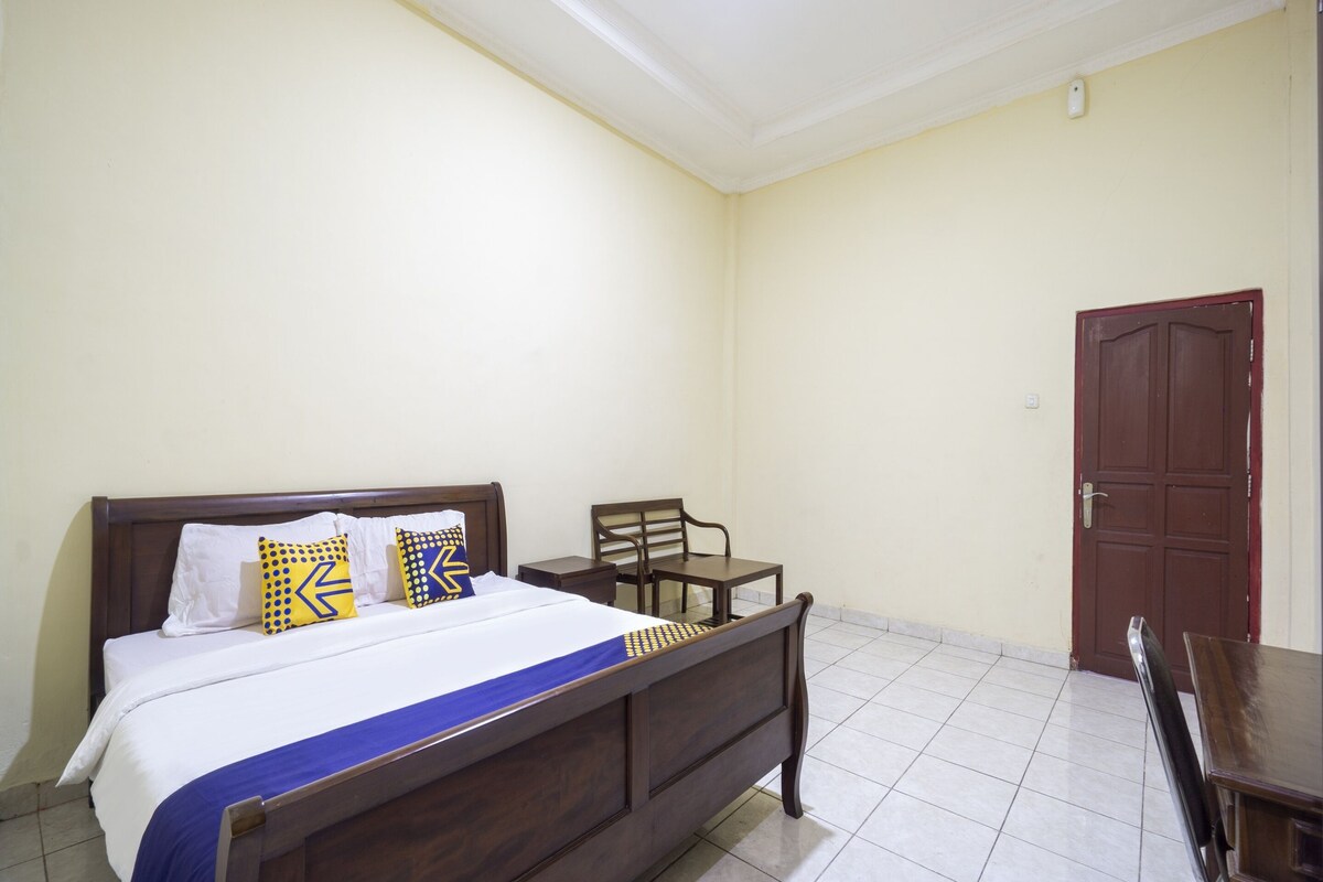 A bedroom with a wooden bed, a chair, a small table, and a door.