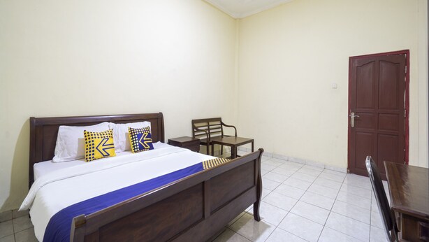 A bedroom with a wooden bed, a chair, a small table, and a door. - Spot ON 3978 Hotel Danau Indah (Bekasi)