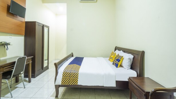 A hotel room with a bed, a desk, a chair, a television, and an air conditioning unit. - Spot ON 3978 Hotel Danau Indah (Bekasi)