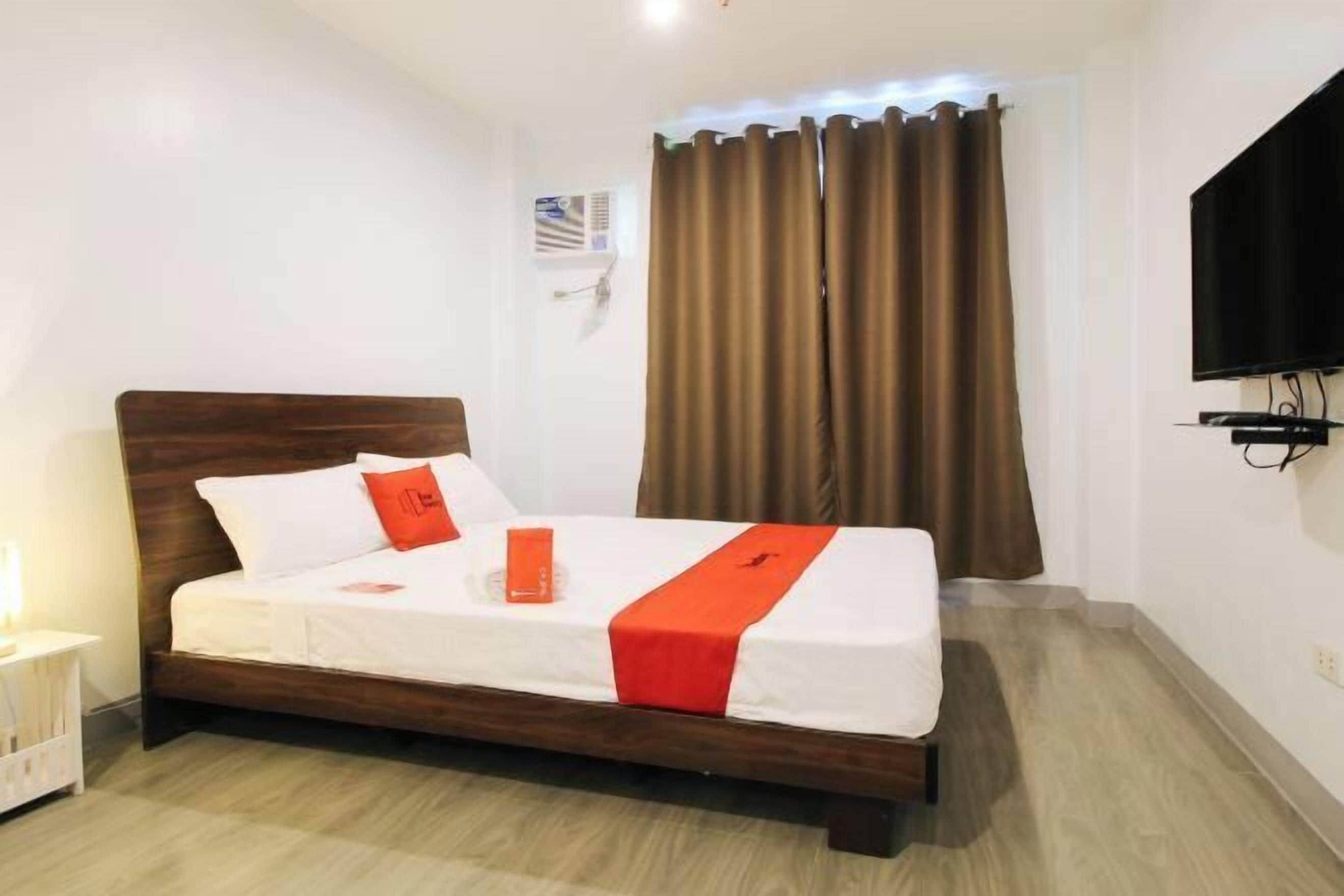 A neatly made bed with a wooden headboard, white bedding, and a red accent.