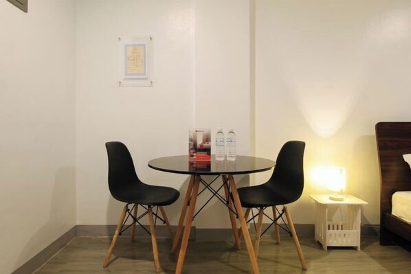 Une petite pièce moderne avec une table ronde et deux chaises noires, une table de chevet avec une lampe et un certificat encadré accroché au mur.