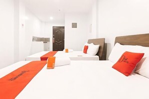 Une chambre d’hôtel avec deux lits, chacun agrémenté de draps blancs et de touches de couleur orange. Un des lits est doté d’une tête de lit en bois, tandis que l’autre a une tête de lit plus simple. Les murs de la chambre sont blancs et une porte est visible au fond.