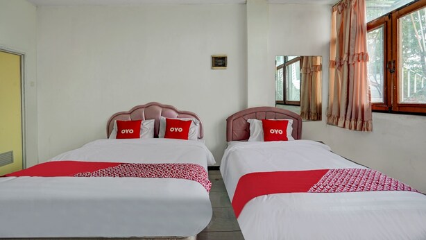 Ein Hotelzimmer mit zwei Betten, jeweils mit einer rot-weißen Musterdecke und Kissen mit dem Aufdruck 'OYO'.