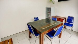 A dining area with a glass-top table, blue chairs, a wooden cabinet, and a television on the wall. - Super OYO 3767 Permata House (Jakarta)