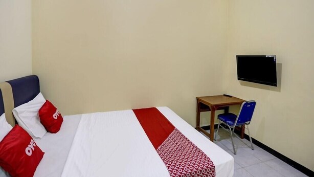A hotel room with a bed, a desk, a chair, and a TV mounted on the wall. - Super OYO 3767 Permata House (Jakarta)