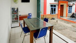 A dining area with a glass table and blue chairs, a refrigerator, and a television on the wall. - Super OYO 3767 Permata House (Jakarta)