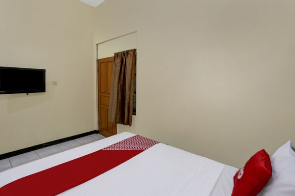 Ein Hotelzimmer mit Bett, Flachbildfernseher an der Wand und einer Holztür mit Vorhängen.