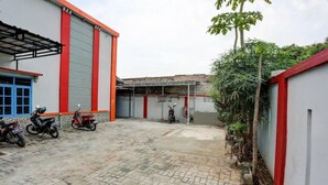 A paved courtyard with a building featuring red and grey walls, a covered area, and several parked motorcycles. - Super OYO 3767 Permata House (Jakarta)