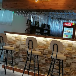 A bar area with stone walls, a Coca-Cola refrigerator, and three bar stools.
