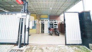 Une entrée fermée par un portail, avec un espace abrité, deux motos garées à l’intérieur et un panneau indiquant « Résidence indienne ».
