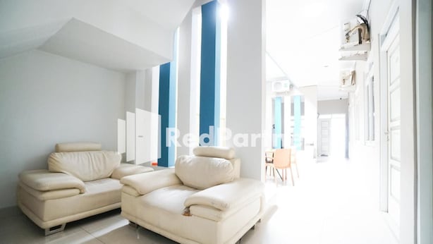 Un salon moderne avec deux canapés beige, un coin repas avec une table et des chaises, et un espace lumineux et aéré doté de grandes fenêtres et d’un plafond haut.