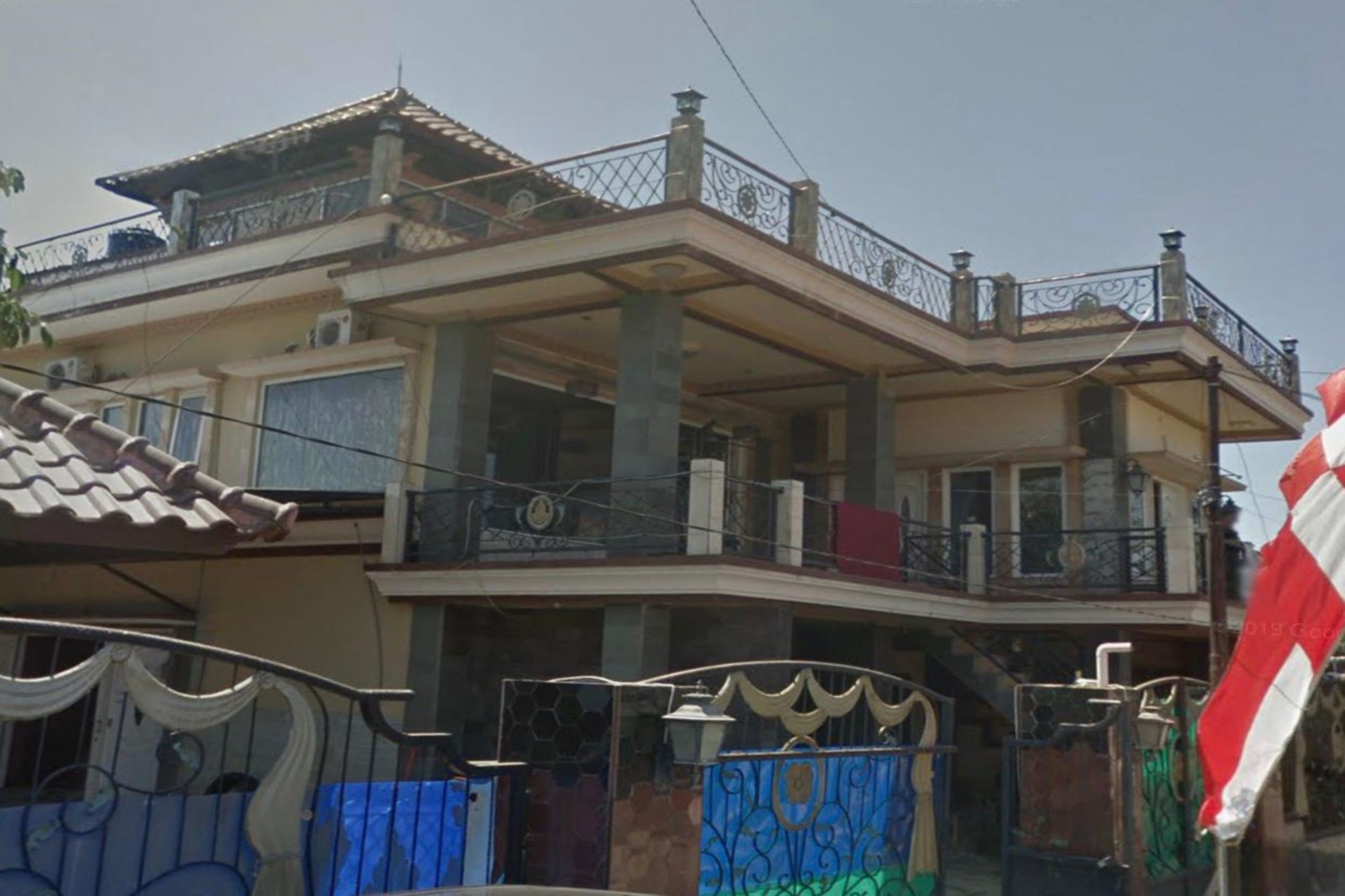 A two-story house with a balcony, a gated entrance, and a flag.