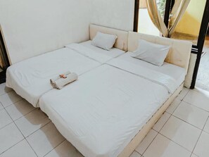 Une chambre avec un lit simple, recouverte d’une courtepointe blanche, avec deux oreillers et une serviette enroulée posée sur le lit.