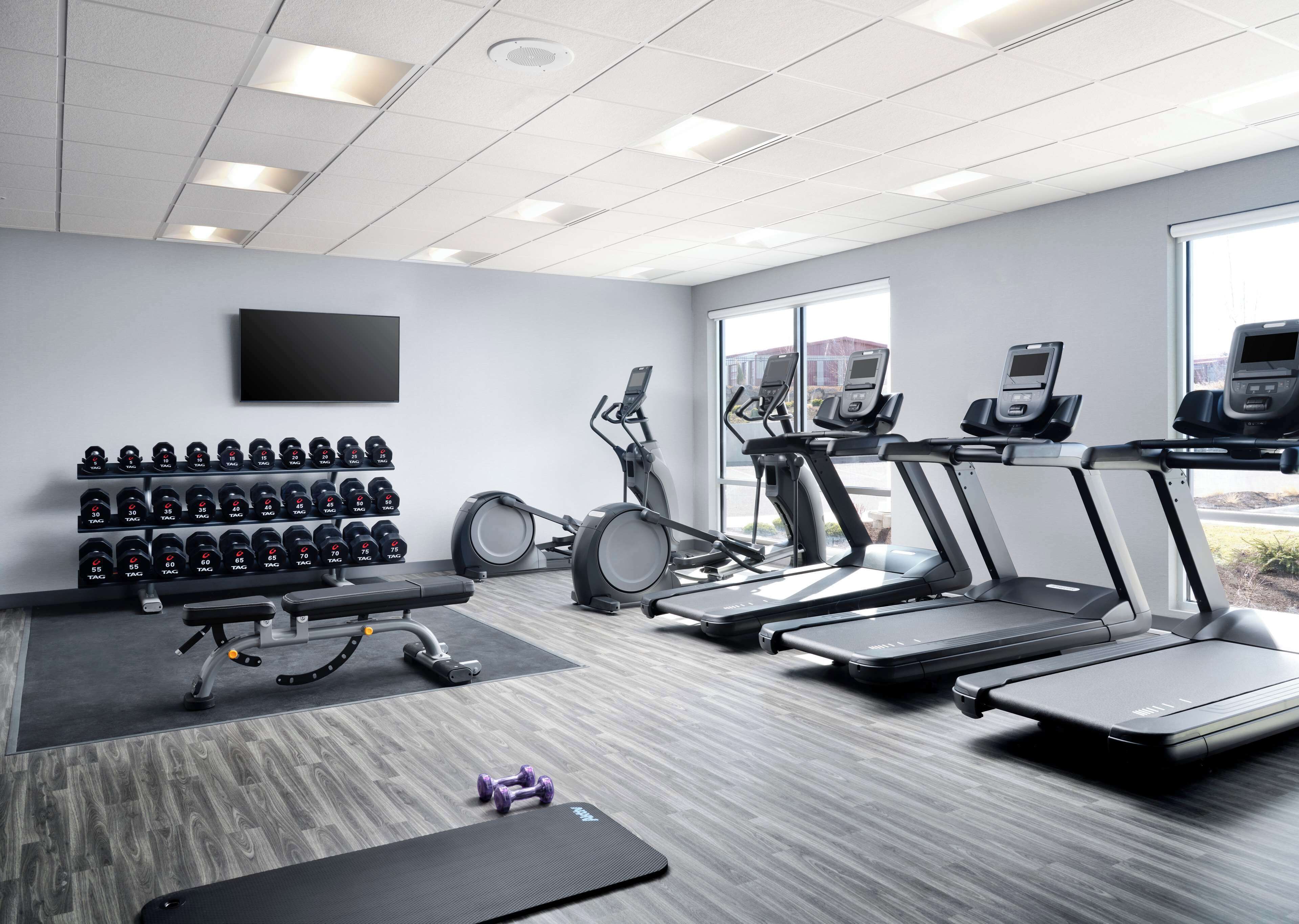 Un gimnasio moderno con cintas de correr, elípticas y una prensa de banca.