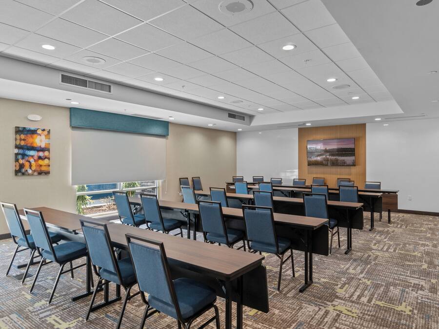 A conference room with multiple tables and chairs, a projector screen, and a large window with a view.