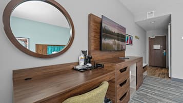 Ein Hotelzimmer mit Schreibtisch aus Holz, einem großen Spiegel, einem Flachbildfernseher und einem Gemälde an der Wand.