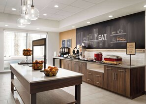 A modern kitchen with a breakfast bar, fruit baskets, and a chalkboard menu.