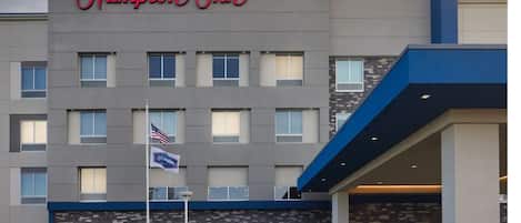 A Hampton Inn hotel with a modern facade, multiple windows, and an American flag.