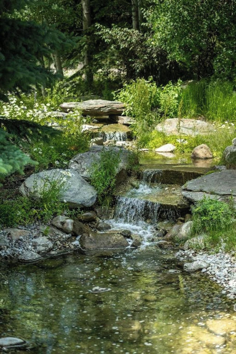 Un cadre naturel en plein air, agrémenté d’une petite cascade, de rochers et de verdure.