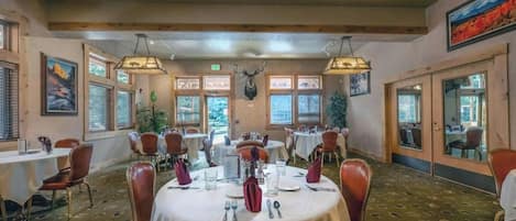 Uma sala de jantar com mesas redondas, cadeiras e um lustre.