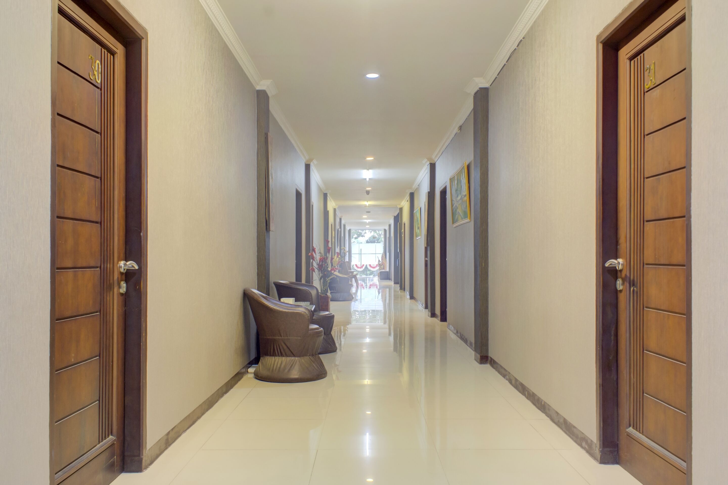 A hallway with wooden doors, a seating area with chairs, and a tiled floor.