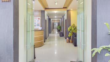 A hotel reception area with a reception desk, a plant, and a corridor leading to other rooms.