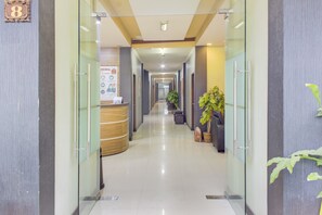 A hotel reception area with a reception desk, a plant, and a corridor leading to other rooms. - OYO 3951 Hotel Tw Rancagoong (Cianjur)