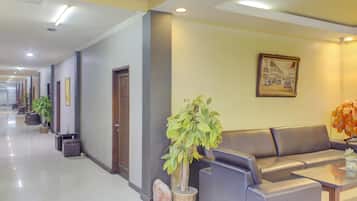 A hotel lobby with a reception area, a sofa, a coffee table, and potted plants.