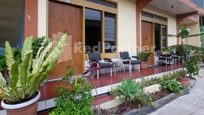 Un hotel con un espacio de estar al aire libre techado, plantas en macetas y un balcón con barandillas.