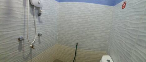 A small bathroom with a toilet, a handheld showerhead, and a wall-mounted faucet.