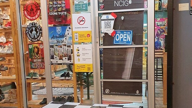 A restaurant with a checkered table and chairs in front, a glass door entrance, and various posters and signs on the glass. - Hotel O Penginapan Wahee (Kuala Terengganu)