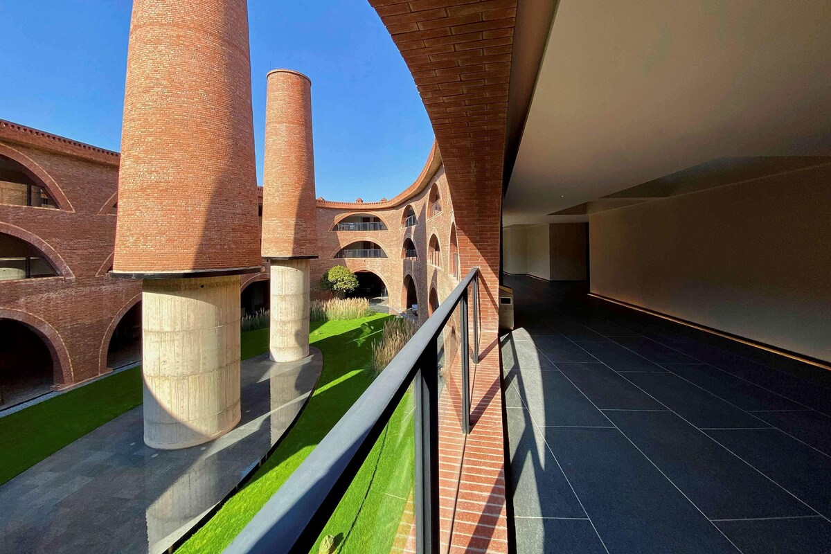 Edifici modern amb arquitectura de maó, estructures cilíndriques grans i un prat verd.